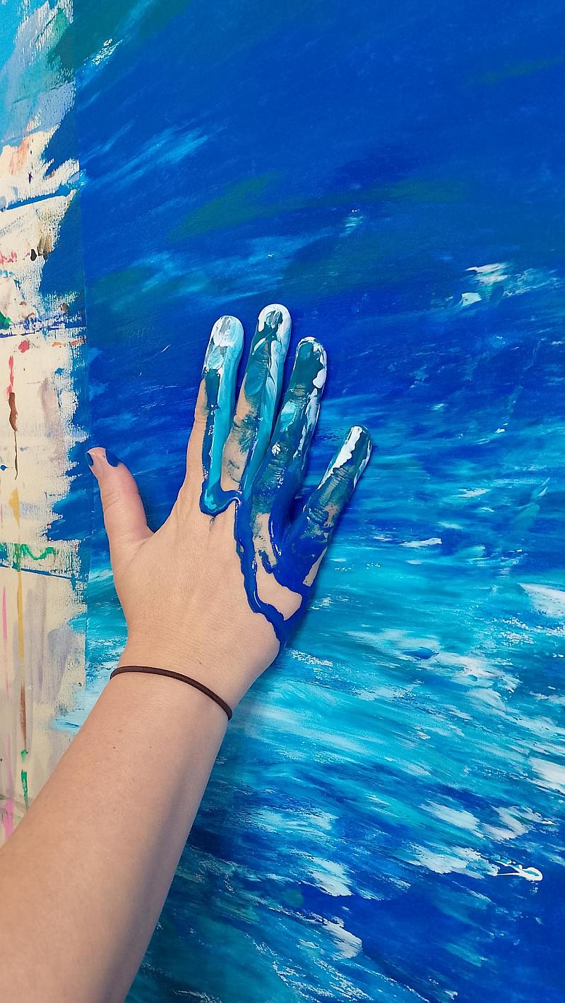 Eine Hand mit blauer Farbe streicht über ein Papier und erzeugt dynamische Muster.